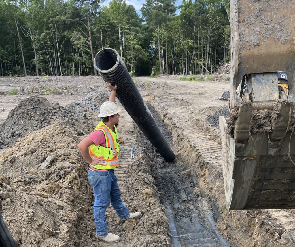 Sitework. Man in construction site directing pipe installation